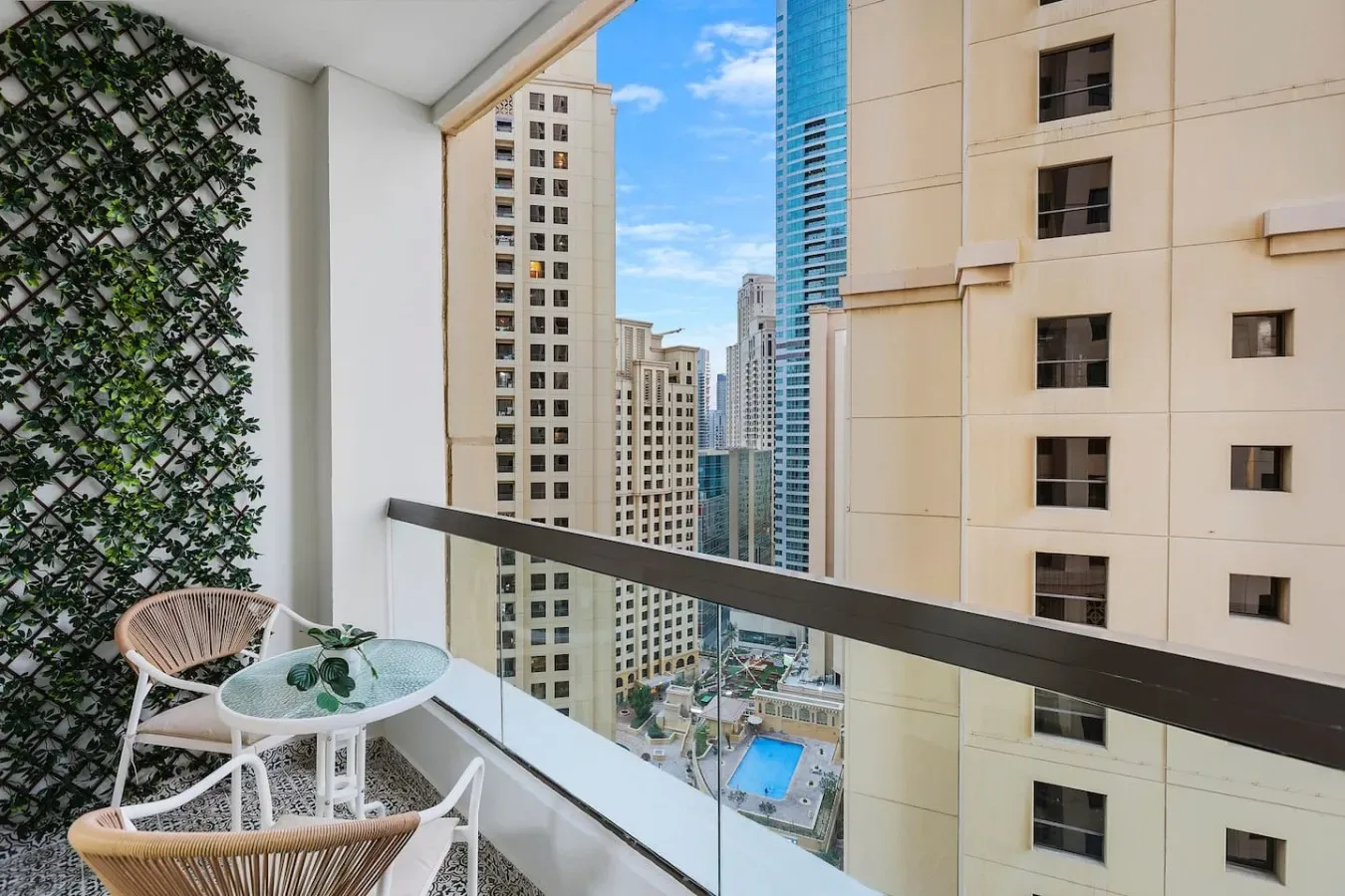 A balcony with seating and a glass railing overlooking nearby high-rise buildings.