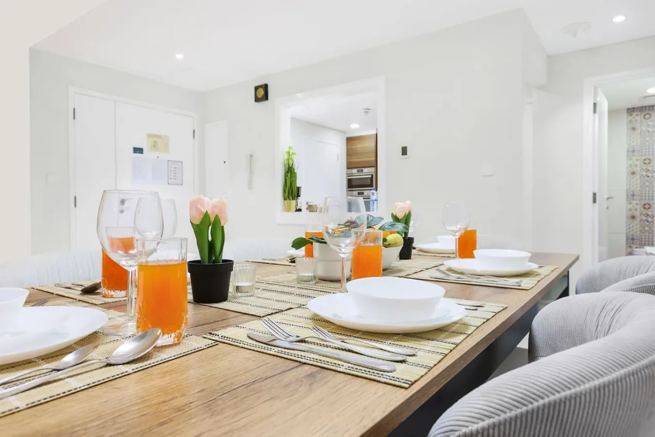 A dining table is set with plates, glasses, and orange juice in a bright room.