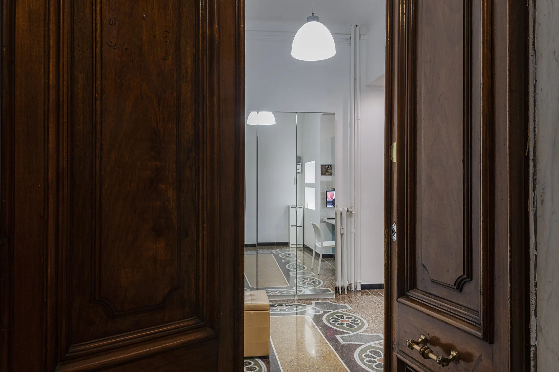 Una puerta de madera abierta deja ver un pasillo iluminado con baldosas estampadas.