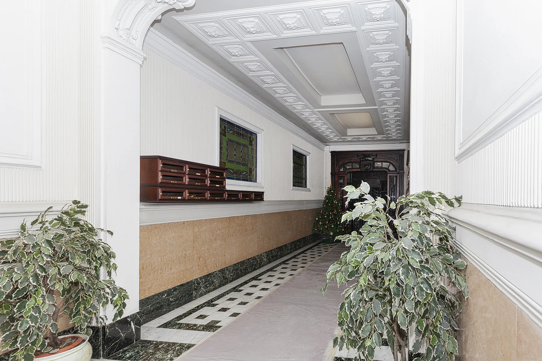 Un pasillo interior decorado con paneles de techo ornamentados y plantas en macetas.