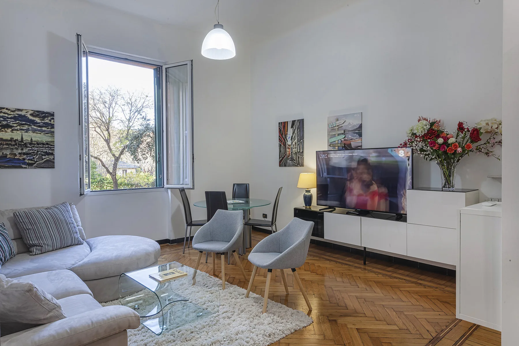 Una sala de estar luminosa con asientos, un televisor y una ventana abierta.