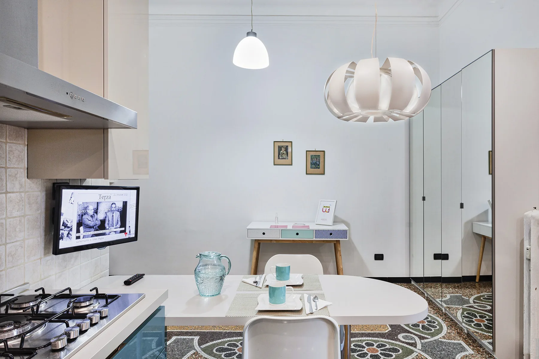 Una cocina y comedor luminosos con una mesa, lámparas colgantes y suelo de baldosas estampadas.