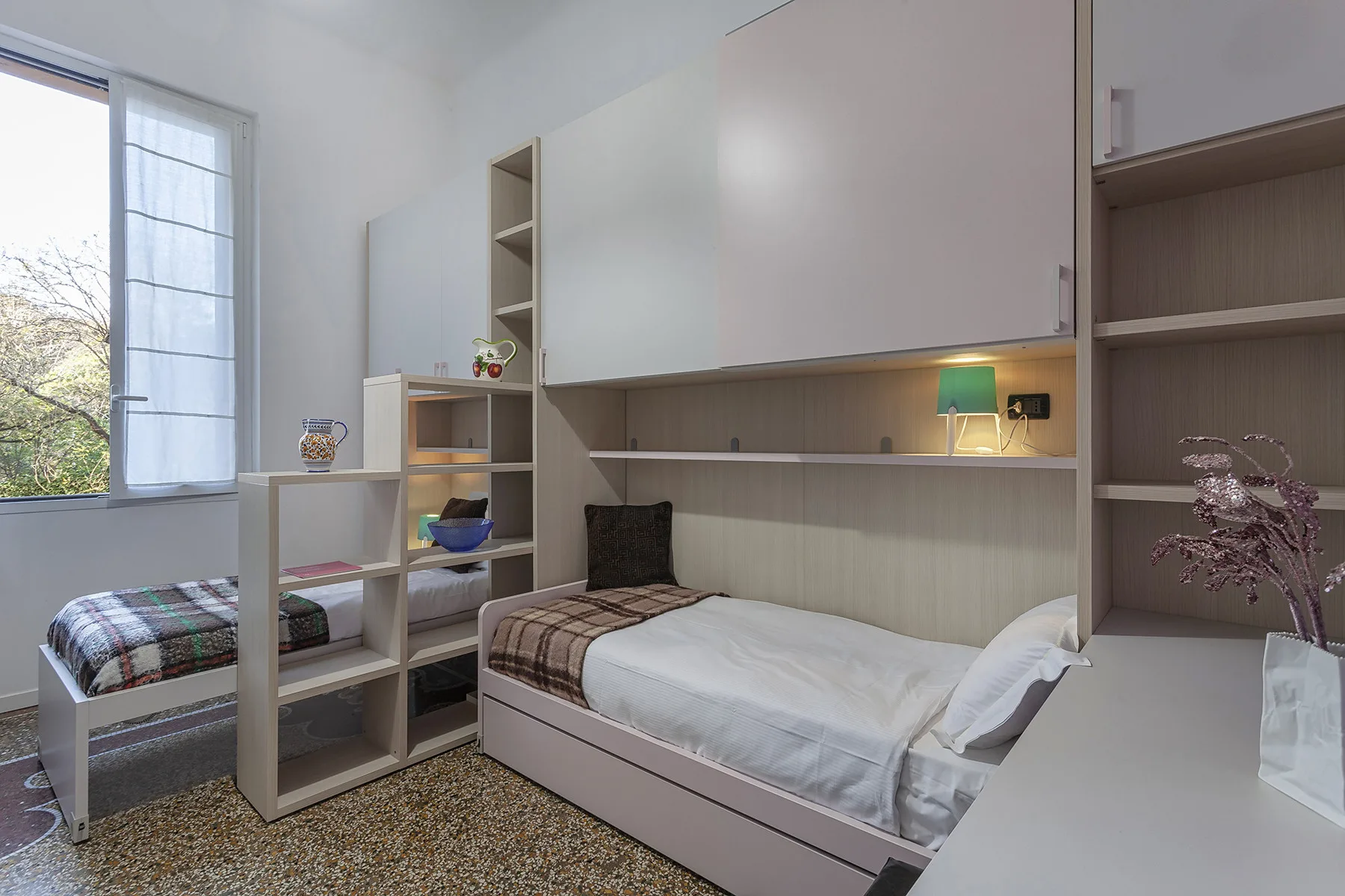 Un dormitorio con dos camas, estanterías abiertas y una ventana grande.