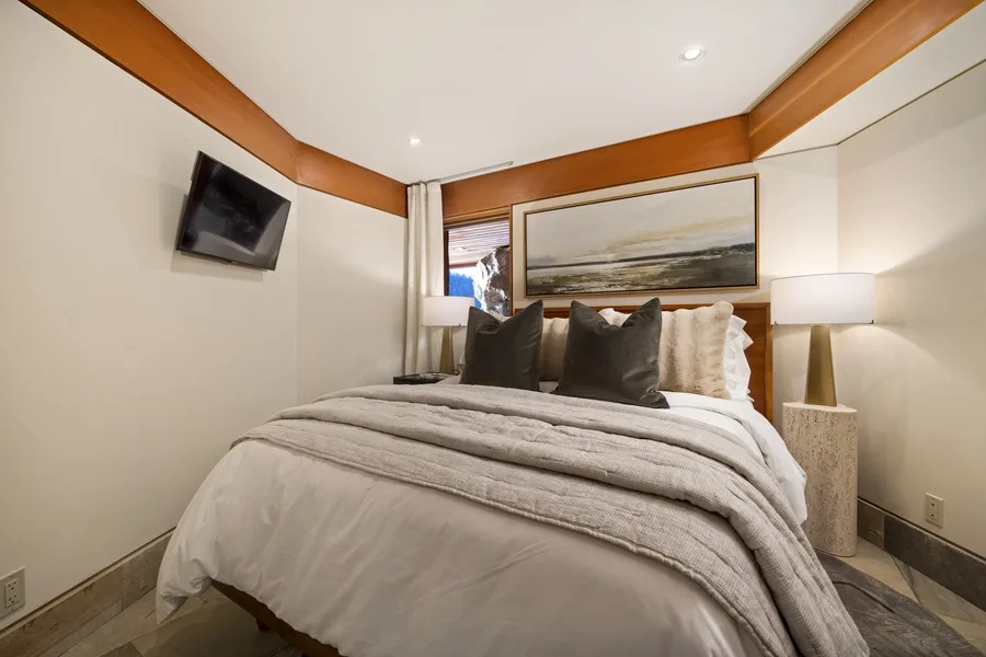 A bedroom with a neatly made bed and a framed landscape above the headboard.