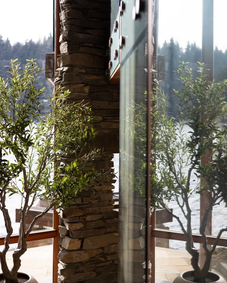 A sunlit indoor area features a stone column and potted plants beside large windows.