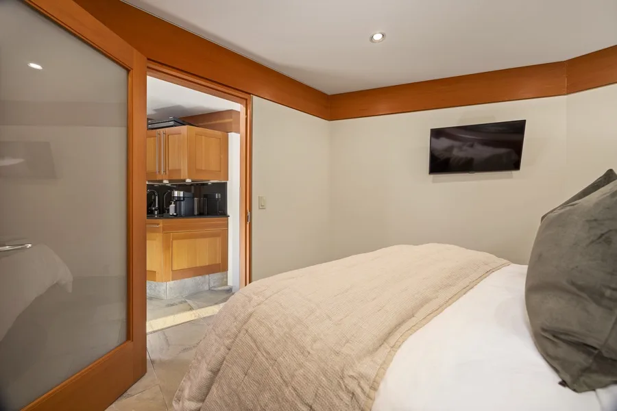 A bedroom with a bed and a kitchenette visible through an open doorway.