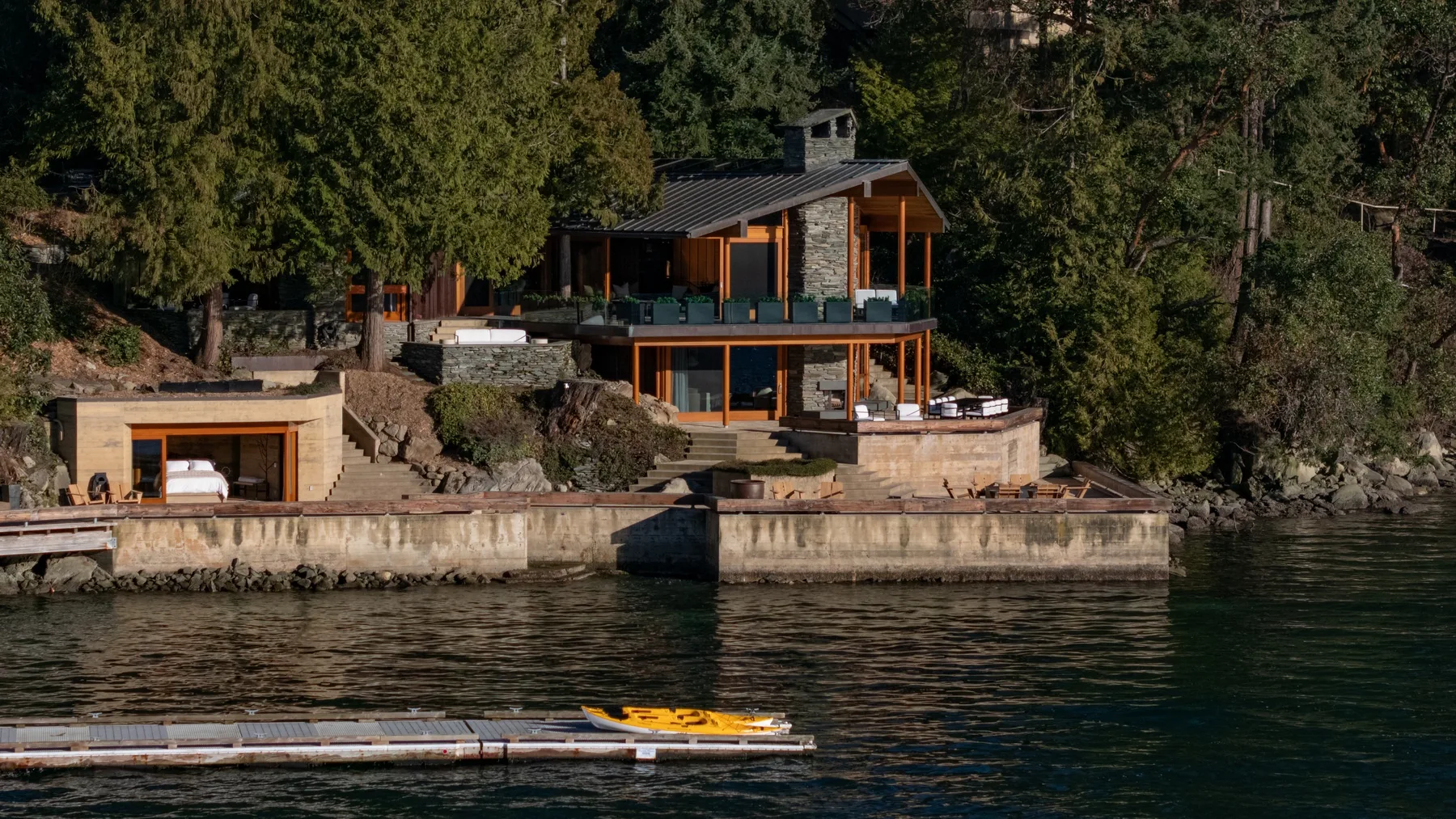 A modern lakeside house sits among trees beside a waterfront dock.