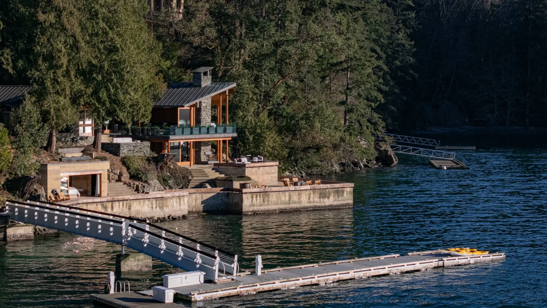 A lakeside house and dock sit beside wooded shoreline.