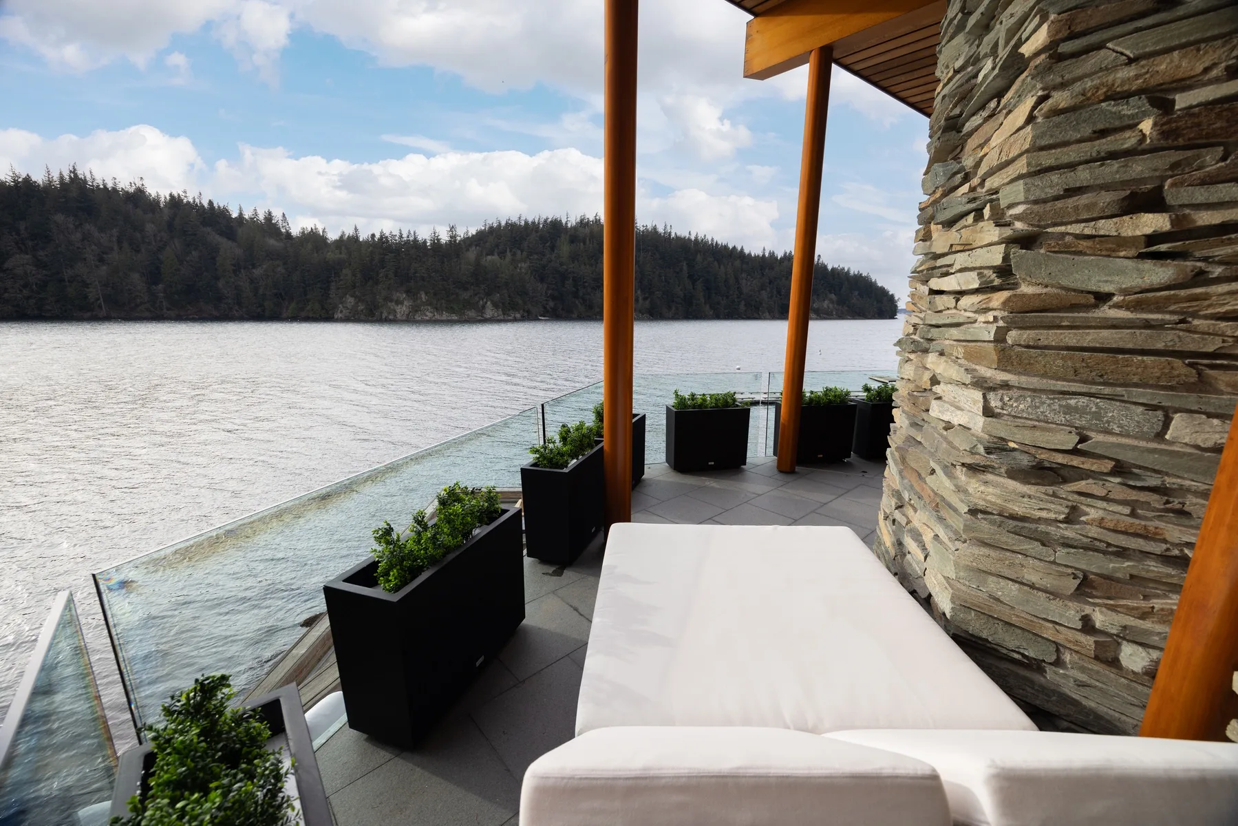 A lakeside terrace with outdoor seating, planters, and a glass railing.