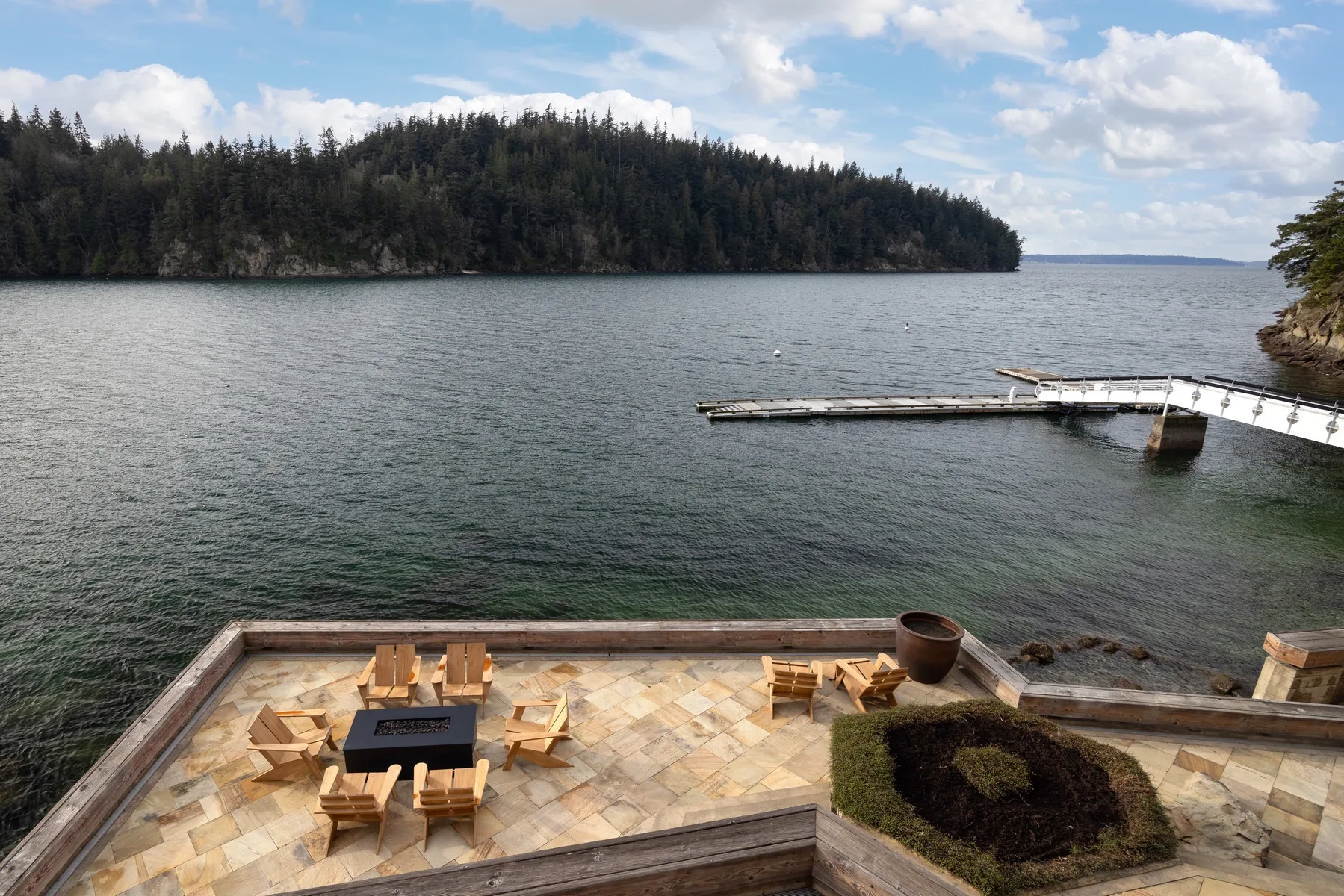 A lakeside patio overlooks a wooded shoreline and a small dock.