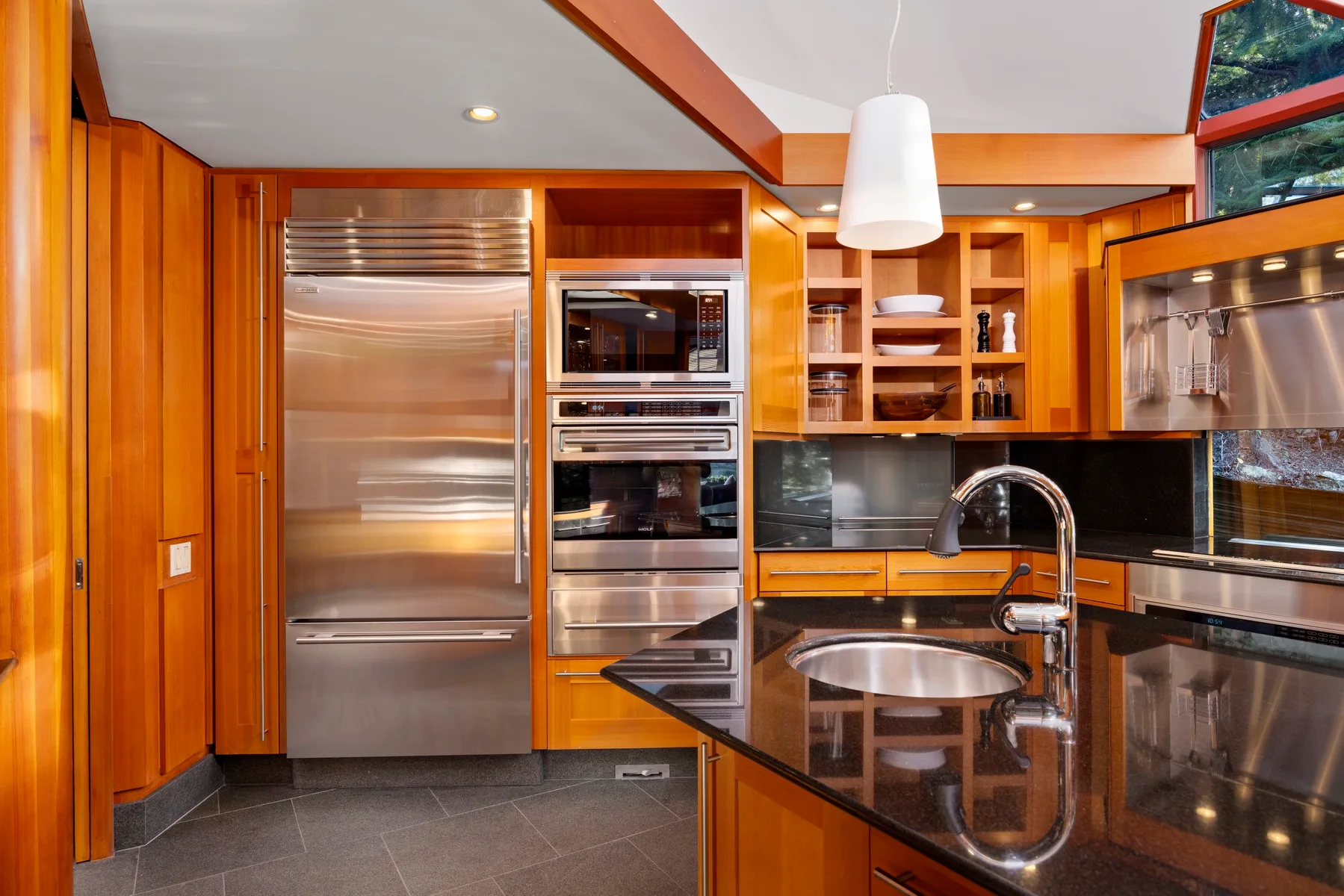A kitchen with warm wood cabinetry, stainless steel appliances, and a dark countertop.