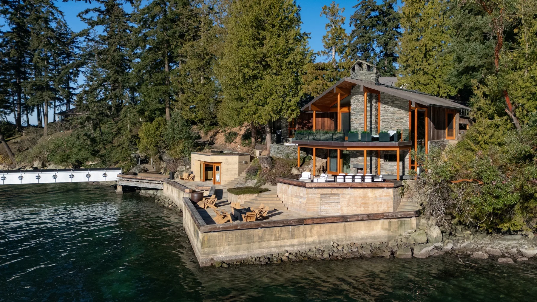 A modern lakeside house overlooks a wooden terrace and dock.