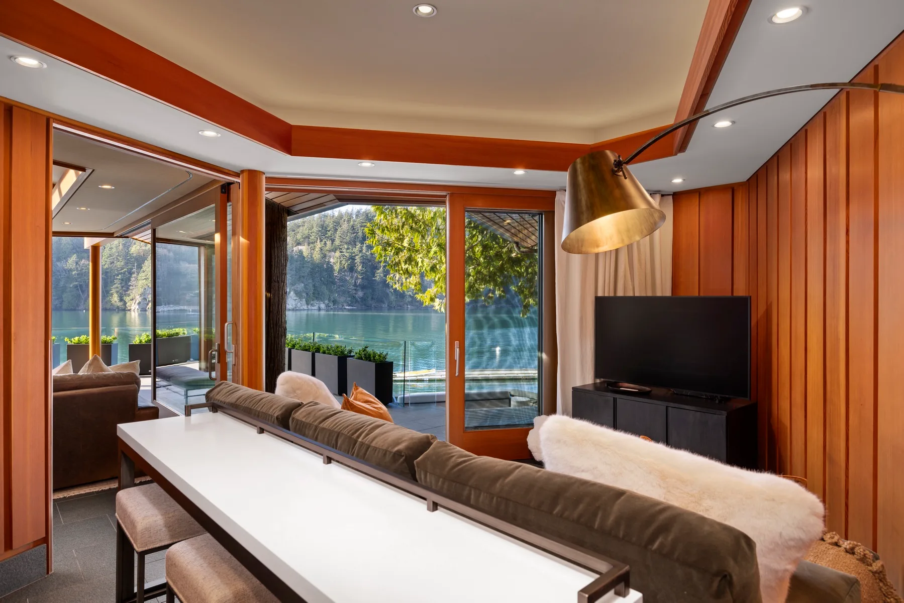 A living room with a long table, seating, and large windows overlooking the water.