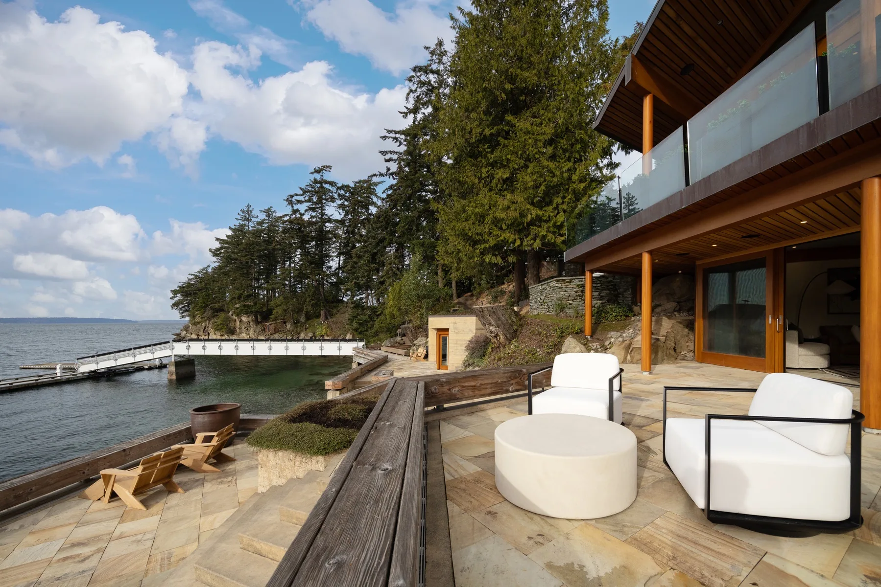 A waterfront patio beside a modern building, with outdoor seating and a view of the water.