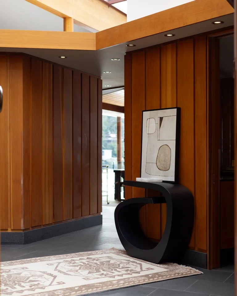 A wood-paneled entryway with a dark sculptural table and framed artwork.