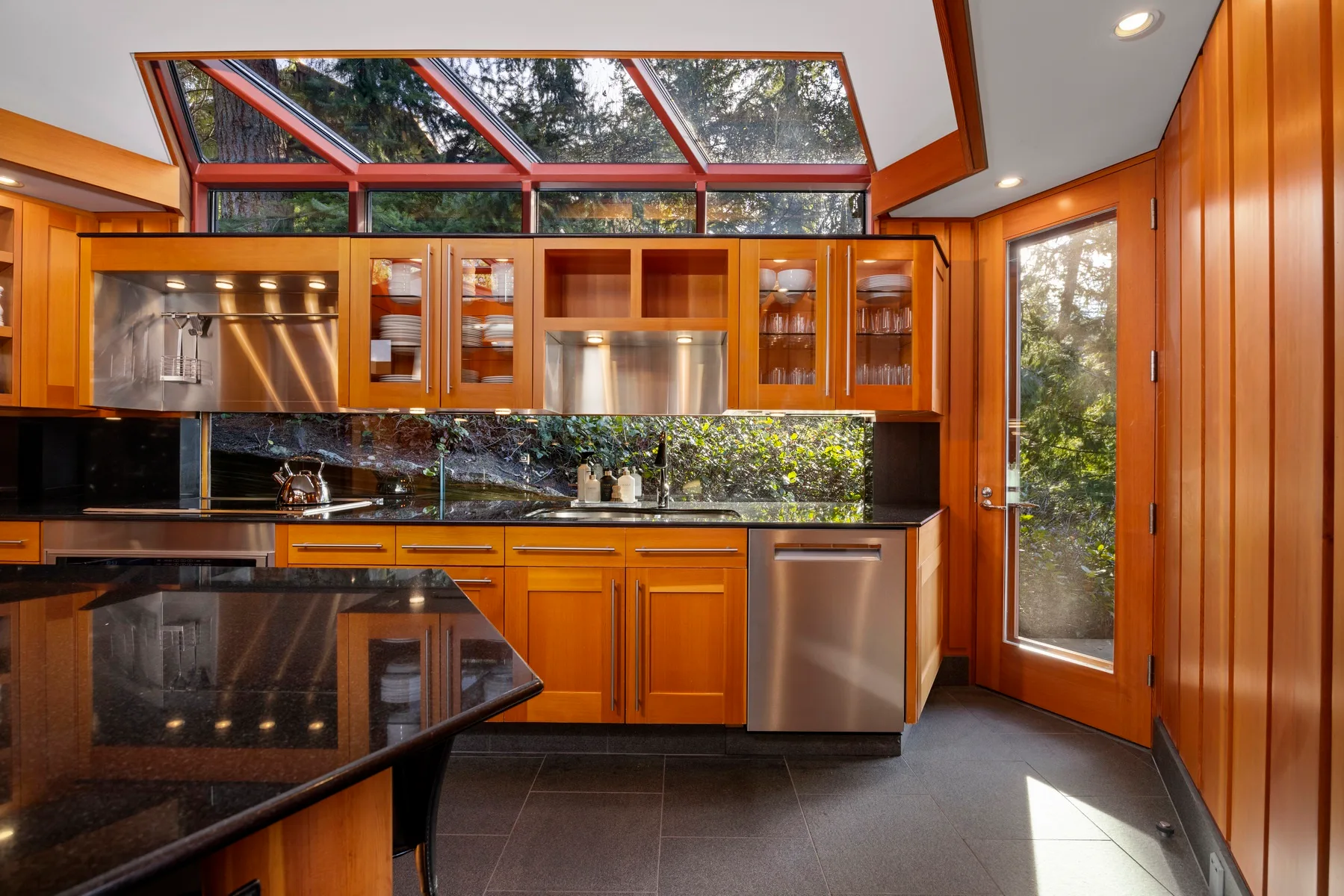 A bright kitchen with orange cabinetry, dark countertops, and tall windows.