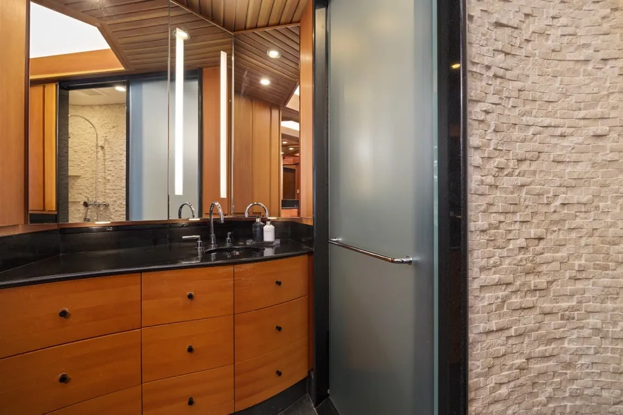 A bathroom vanity with a dark countertop and a frosted glass shower panel.