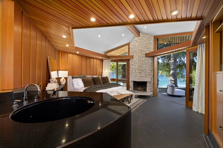 A wood-paneled living room with a seating area, stone fireplace, and large windows.