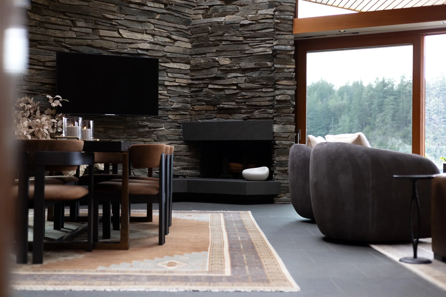 A living room with a dining table, seating, and a stone fireplace wall.