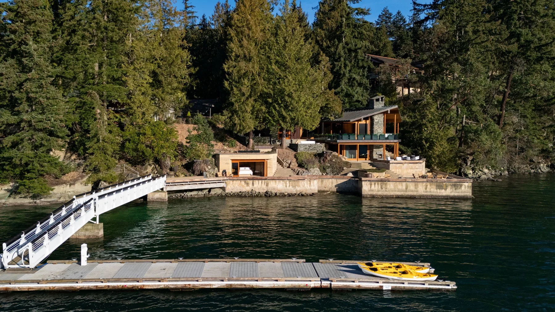 A lakeside property sits among trees, with a dock and white walkway extending over the water.