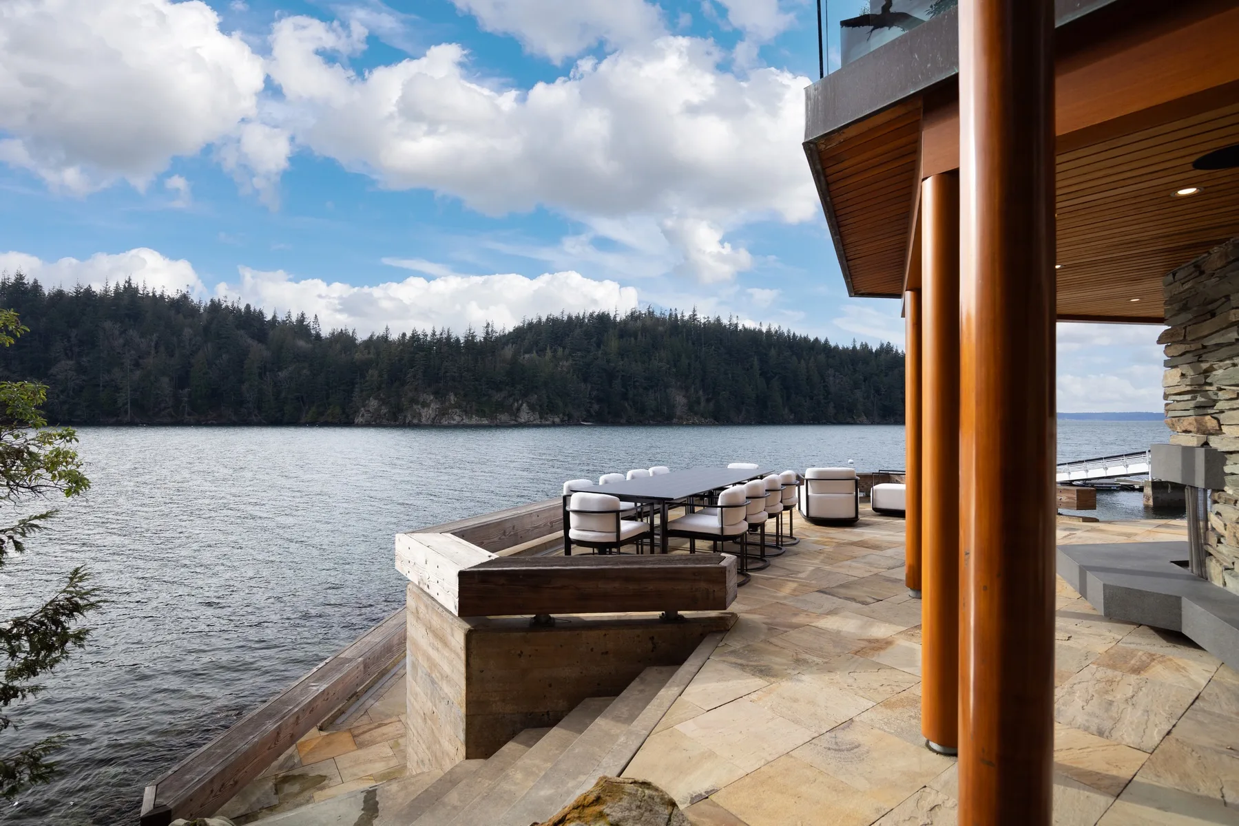A lakeside patio with outdoor seating overlooks the water and wooded shoreline.