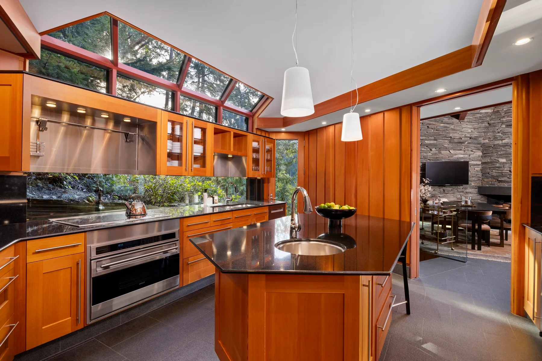 A modern kitchen with orange cabinetry, a central island, and large slanted windows.