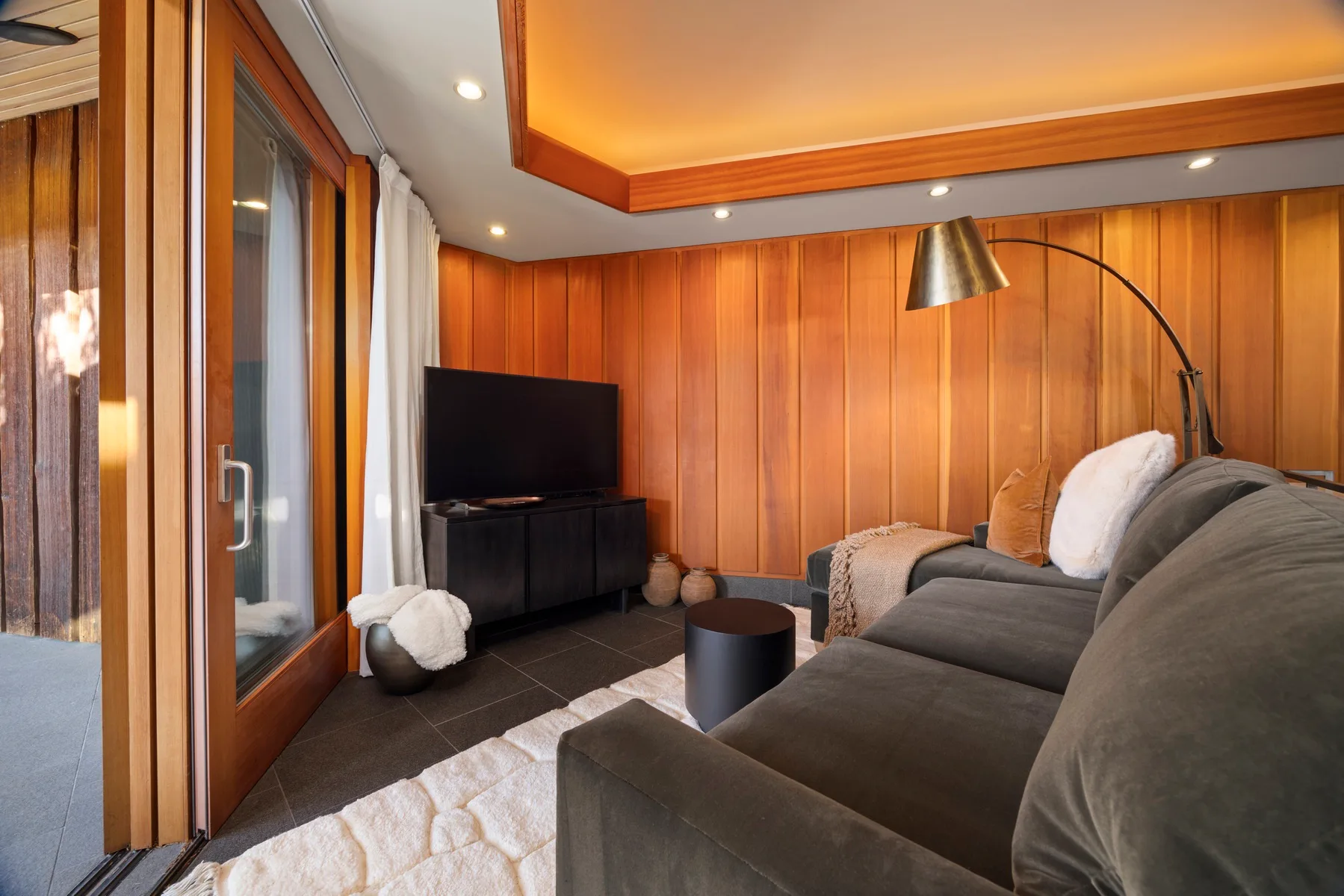 A living room with a sofa, television, and tall glass doors.