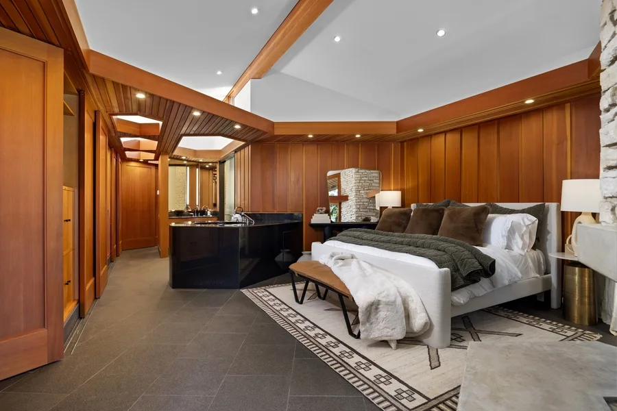 A bedroom with a bed and a dark kitchen island in the background.