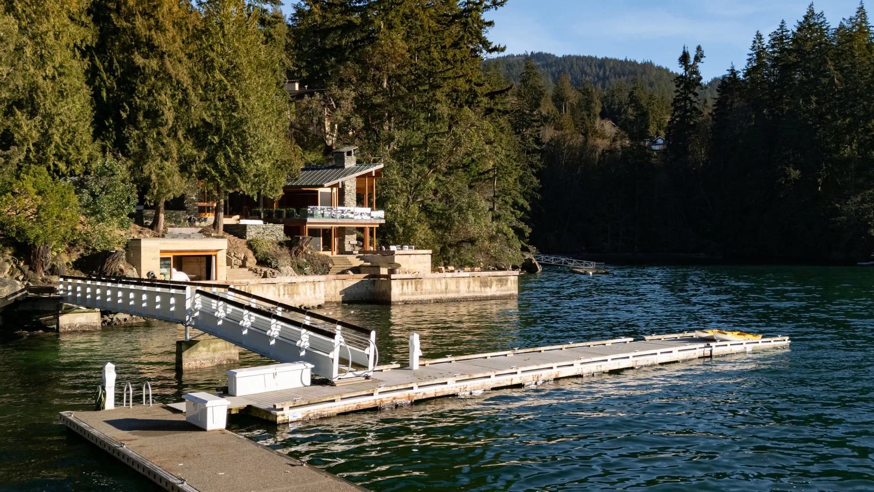 A lakeside house and floating dock sit beside a forested shoreline.