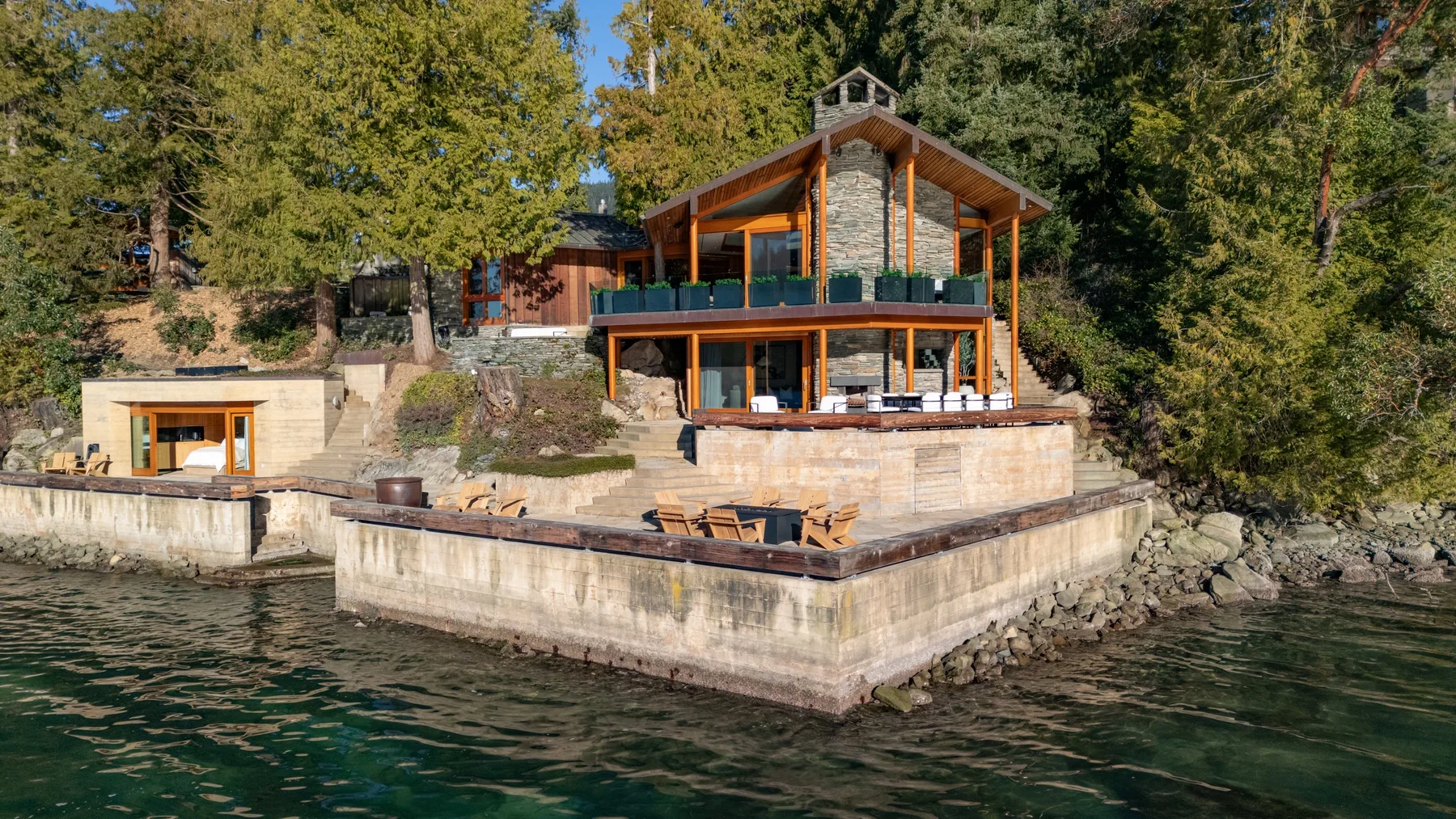 A waterfront house with a stone facade and a broad terrace above the water.