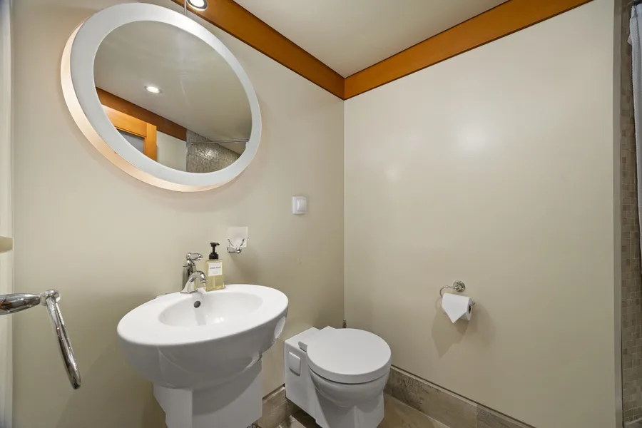 A compact bathroom with a sink, toilet, and round wall mirror.