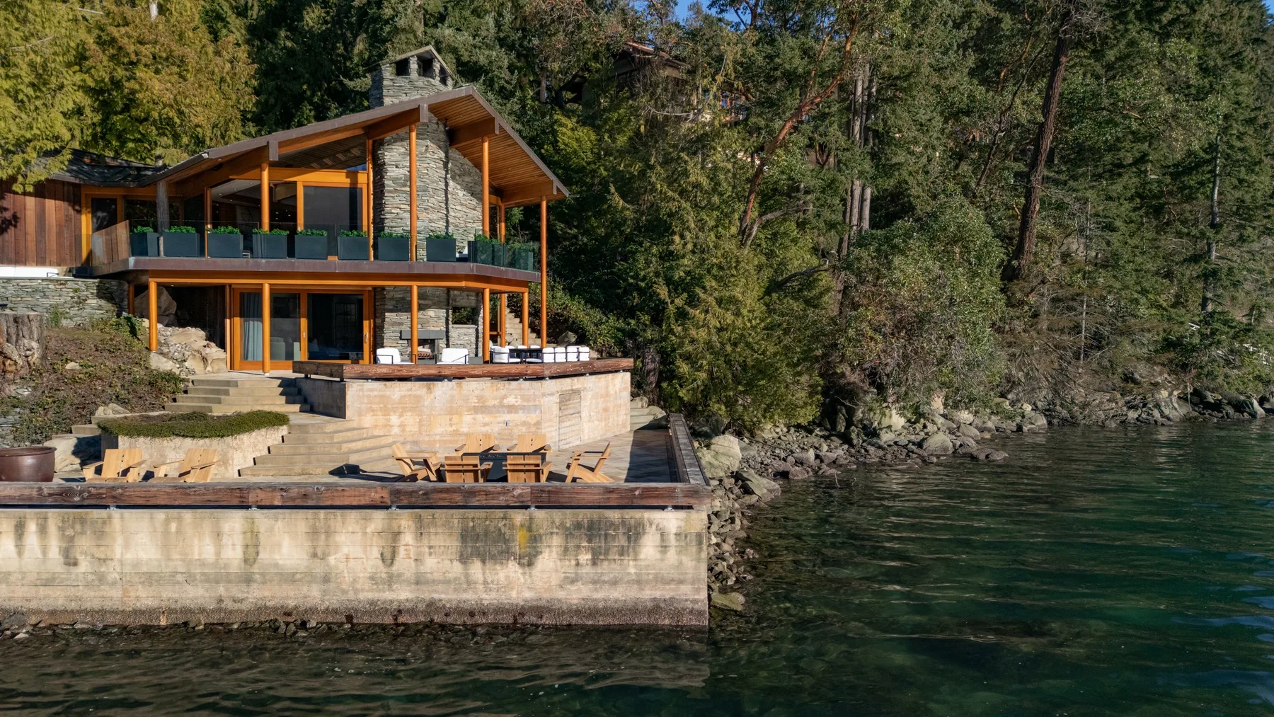A lakeside house with a wooden deck sits beside forested water.