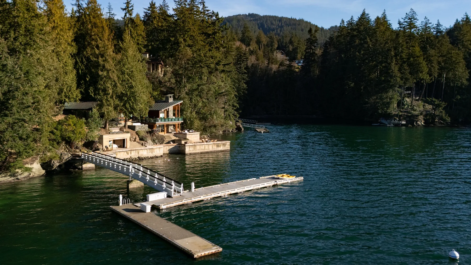 A lakeside dock extends into the water beside a wooded shoreline.