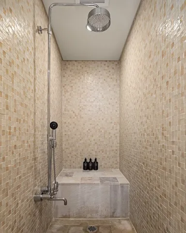 A tiled shower with a rainfall showerhead and a small tiled ledge.