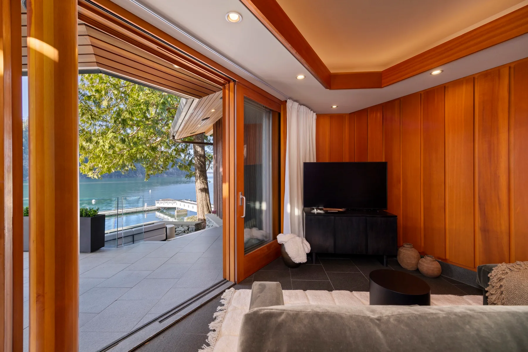 A wood-paneled living room opens onto a terrace overlooking the water.
