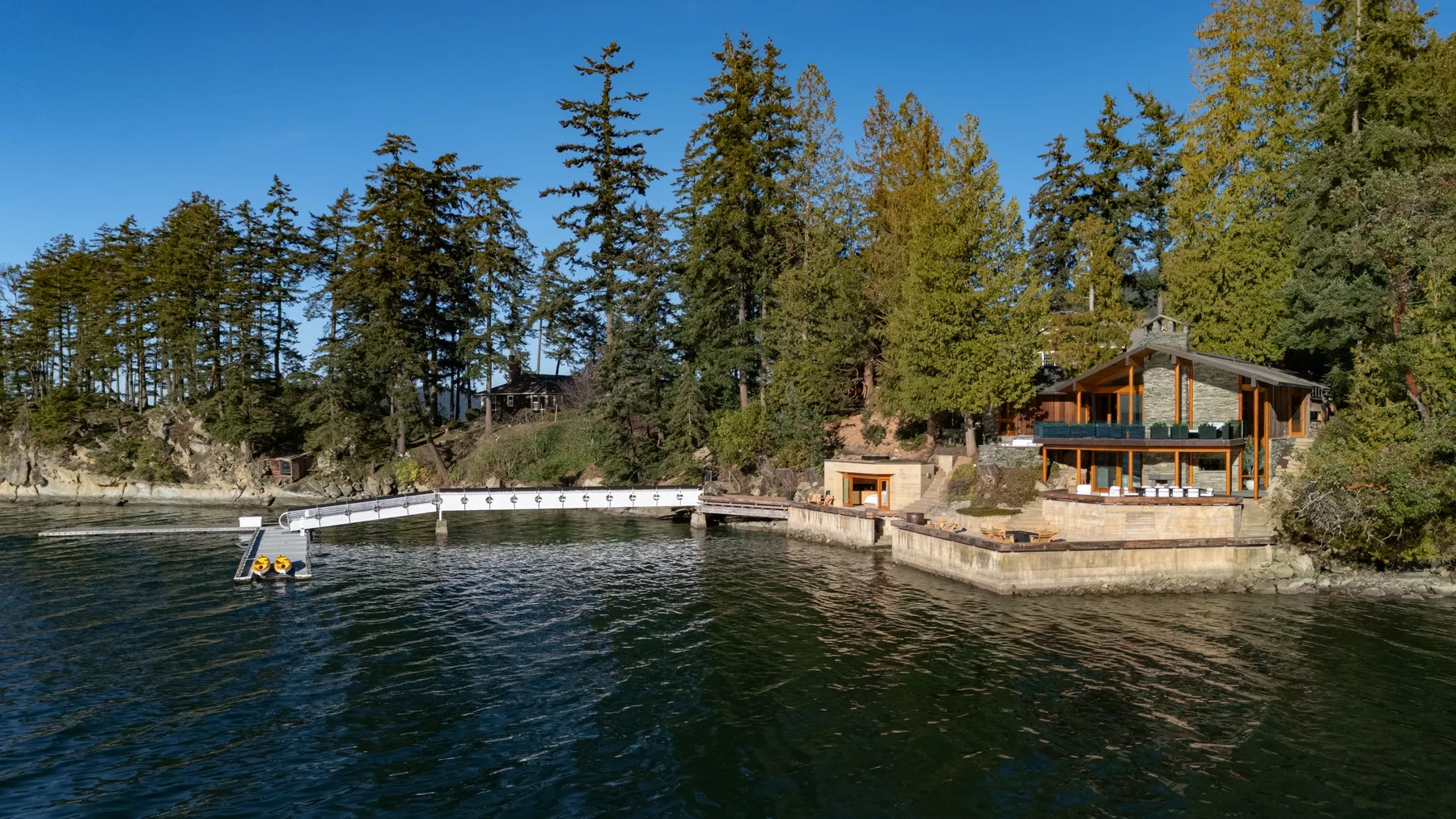 A wooded waterfront property beside a calm inlet and small dock.