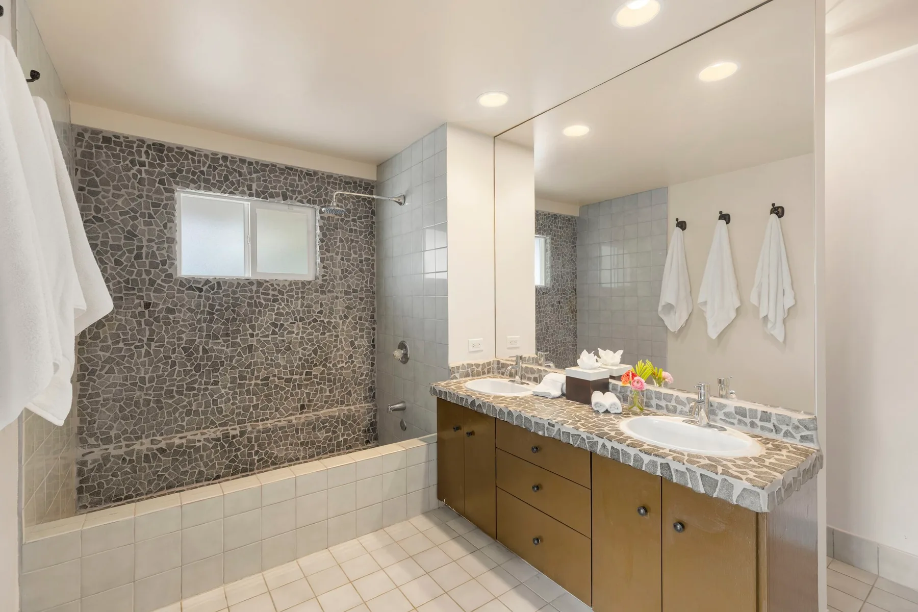 A bathroom with a tiled bathtub and a long vanity beside a large mirror.