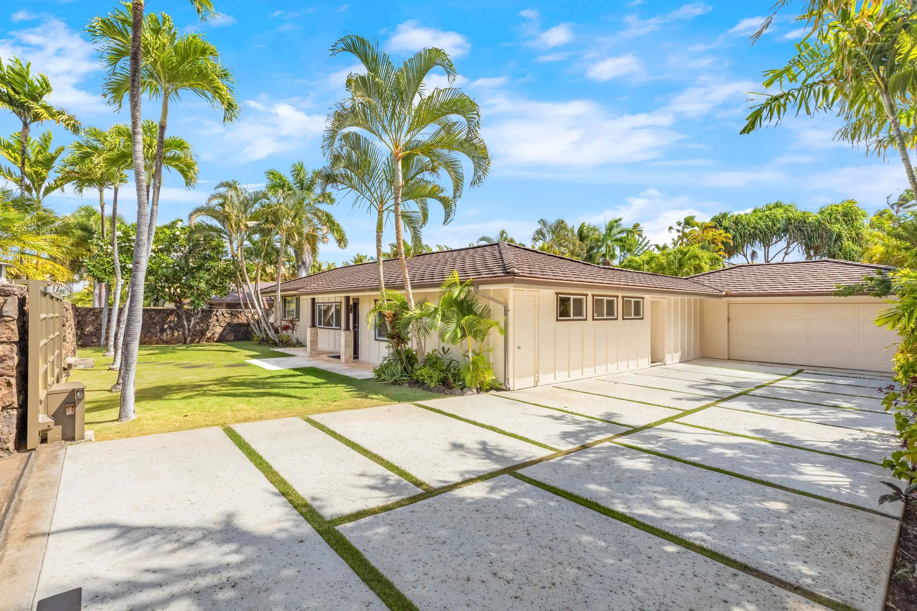 A single-story house with a paved driveway, lawn, and palm trees.