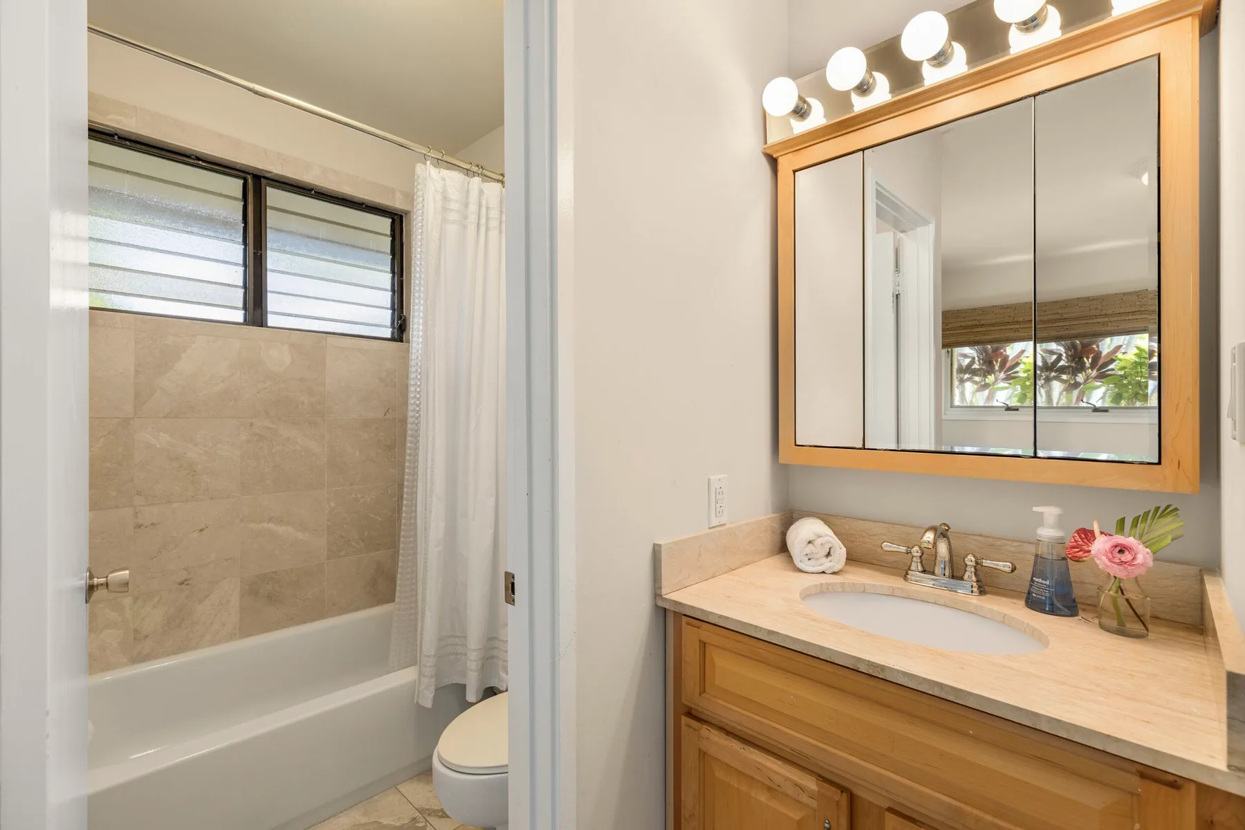 A bathroom with a bathtub, shower curtain, and vanity with a large mirror.