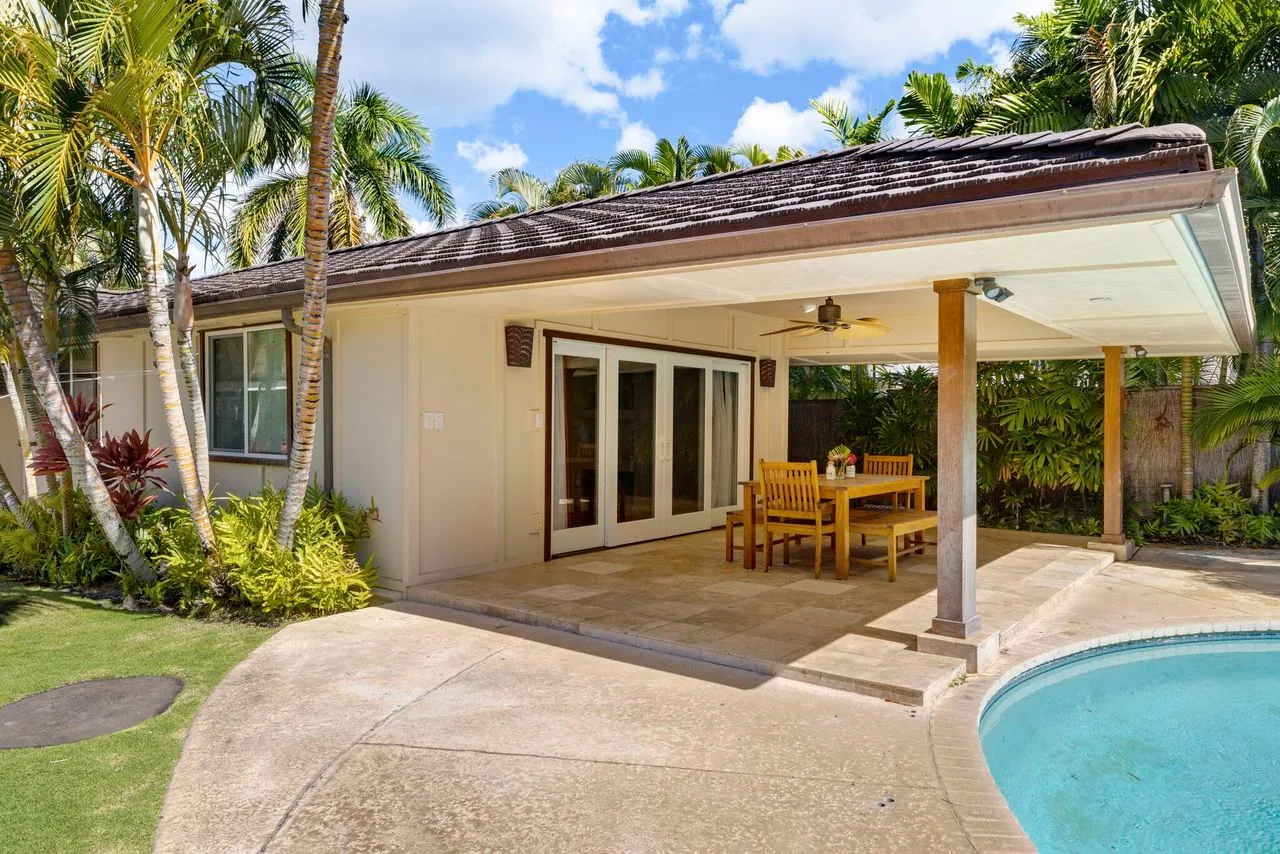 A covered patio with outdoor seating beside a swimming pool.
