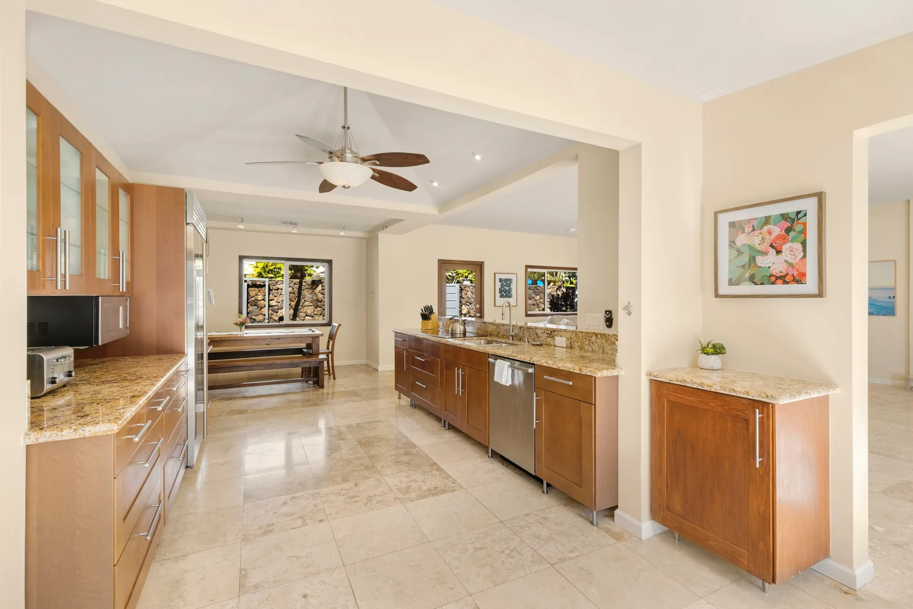 A bright kitchen with wood cabinets, stone countertops, and a dining table in the background.