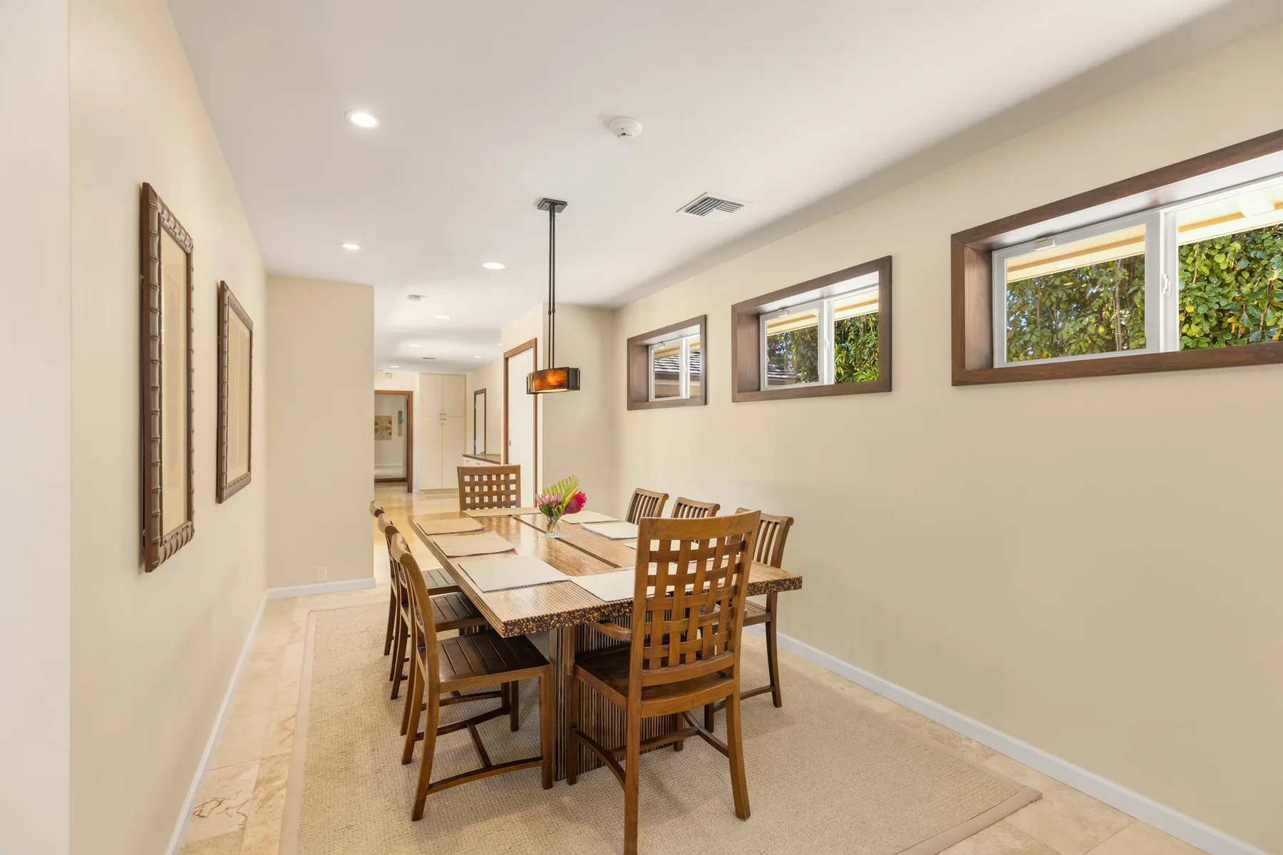 A dining area with a wooden table and chairs beneath several windows.