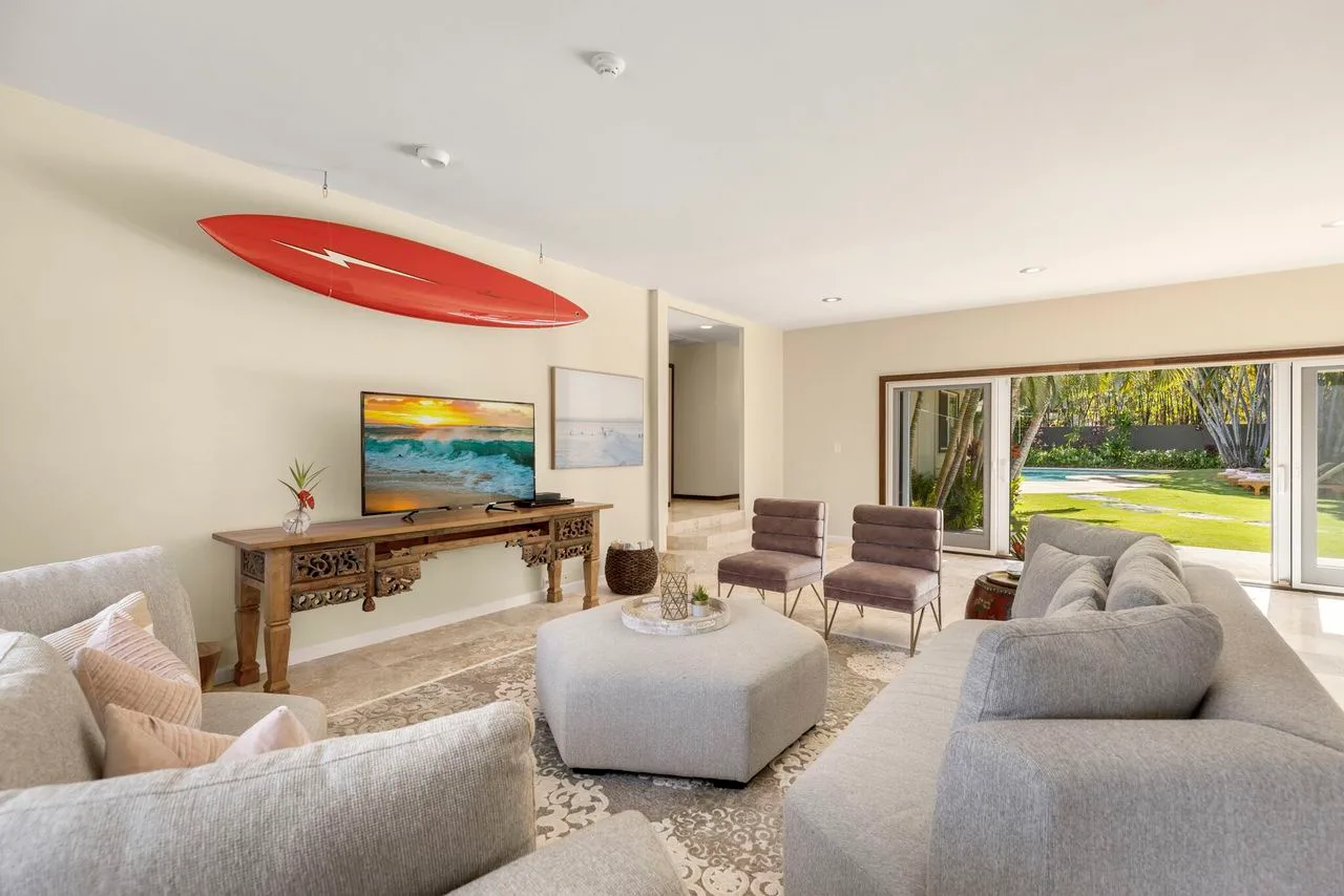 A bright living room has seating around a coffee table and wide windows overlooking a garden.