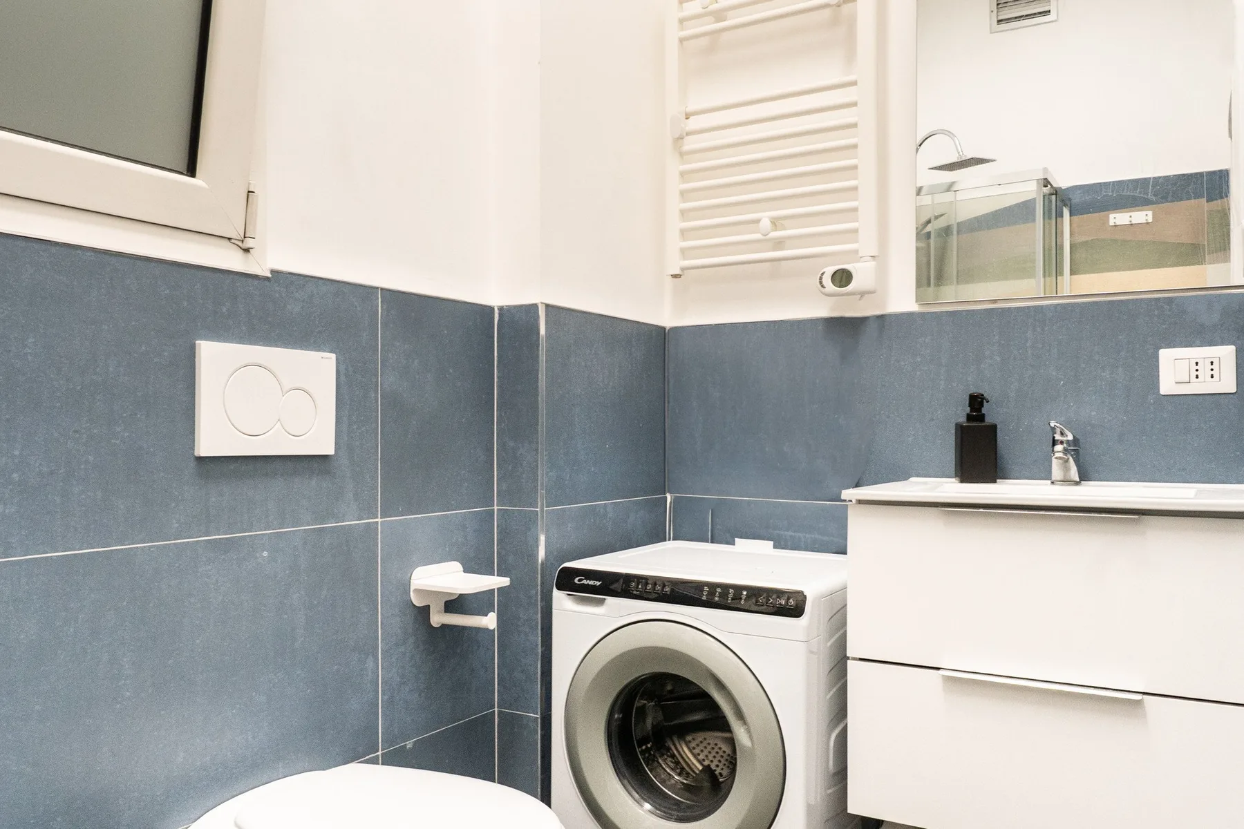 A bathroom with a washing machine beside the sink and shower.