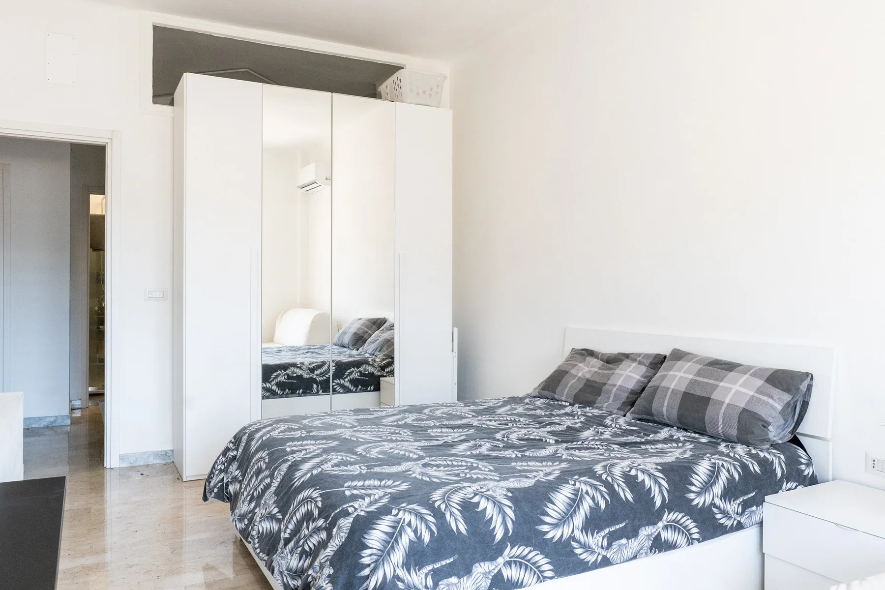 A bedroom with a bed covered in a dark patterned bedspread and a mirrored wardrobe.