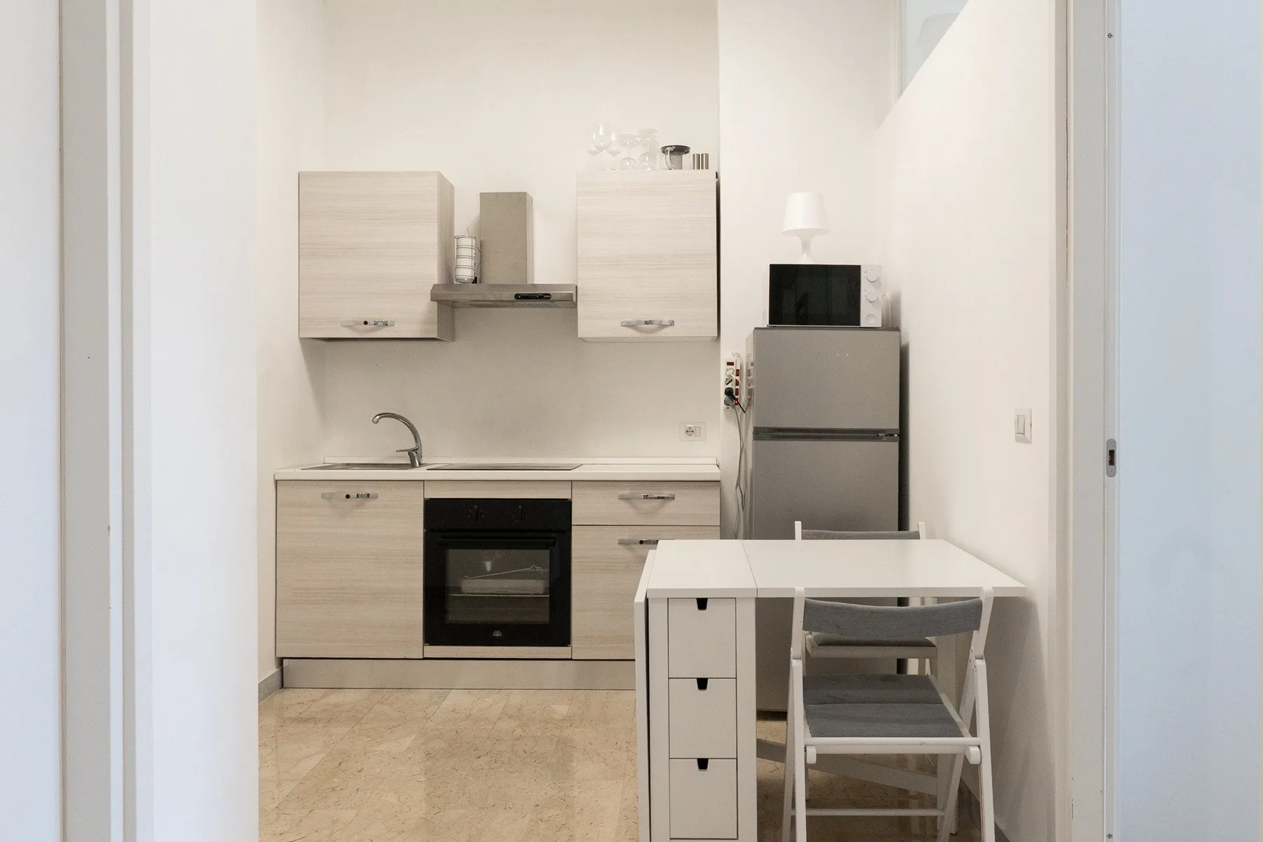 A compact kitchen with light wood cabinets, a refrigerator, and a small dining table.