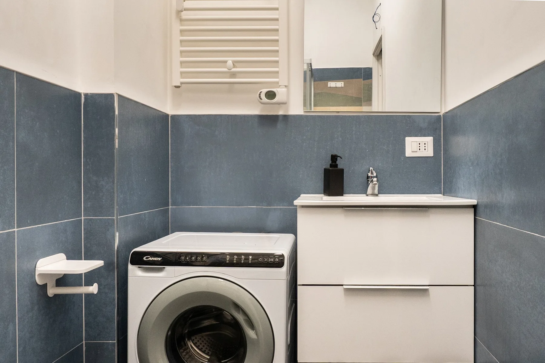 A bathroom with a front-loading washing machine beside a sink cabinet.