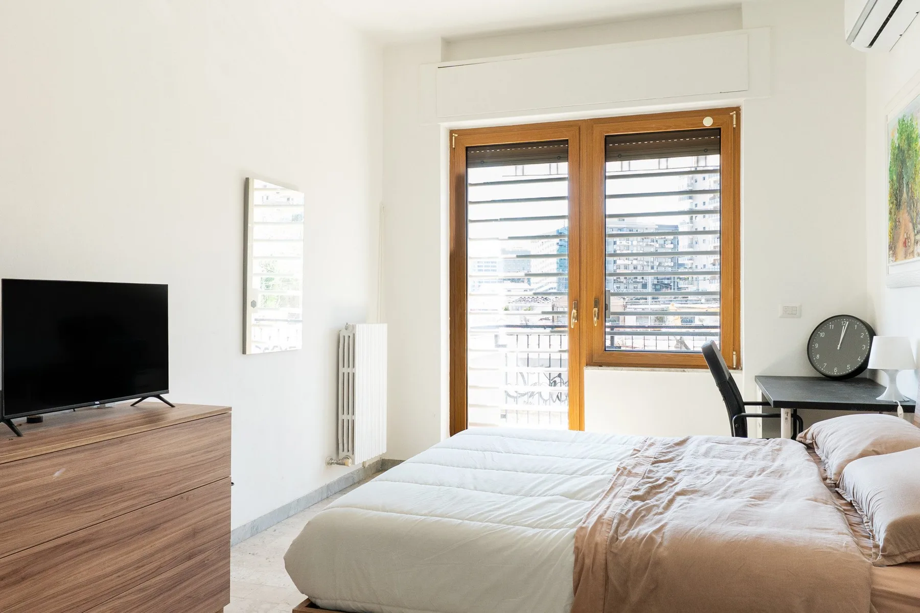 A bright bedroom with a bed beside wooden-framed windows.