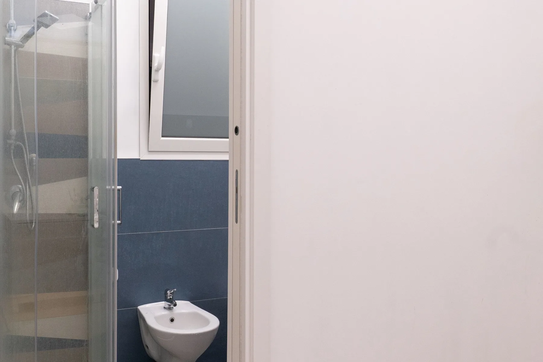 A bathroom with a glass shower, wall-mounted sink, and bidet.