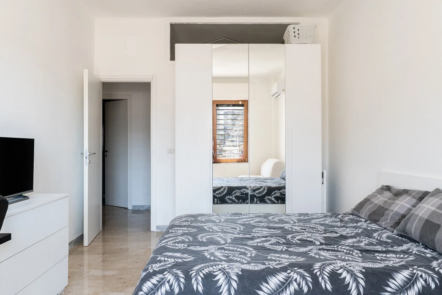 A bedroom with a patterned bedspread and a wardrobe with mirrored doors.